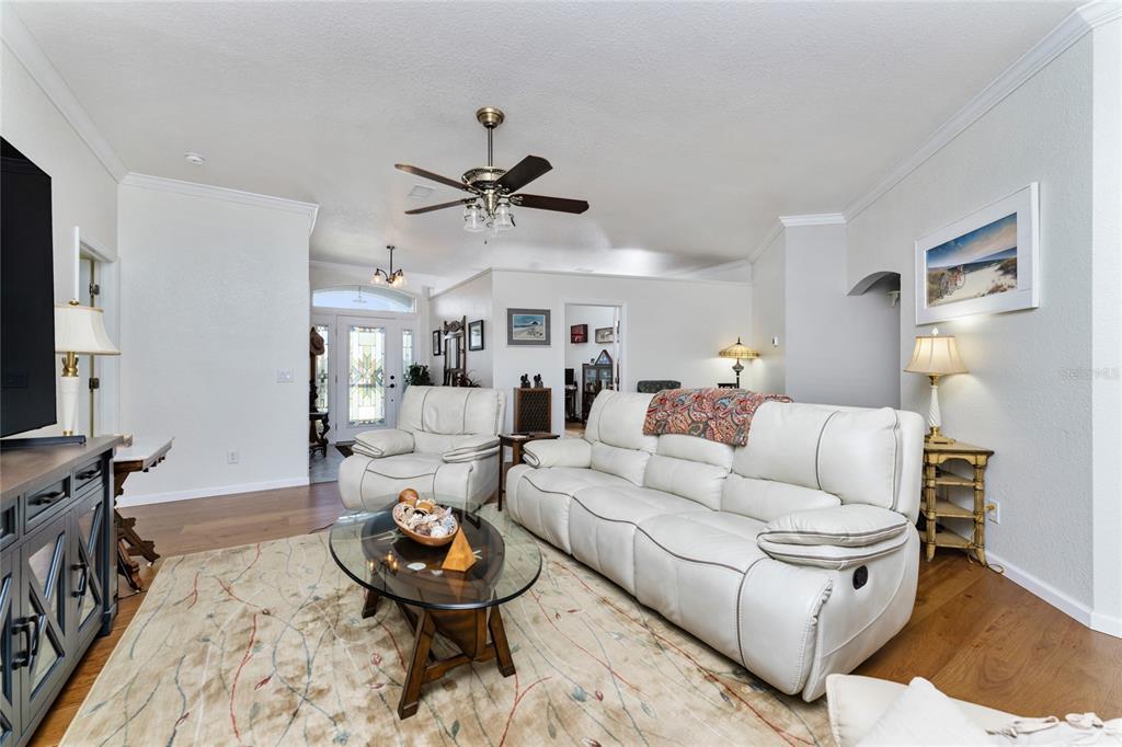 A living room features a white leather sofa, matching armchair, glass coffee table, and hardwood floors — 15105 ALDAMA CIRCLE, PORT CHARLOTTE, FL