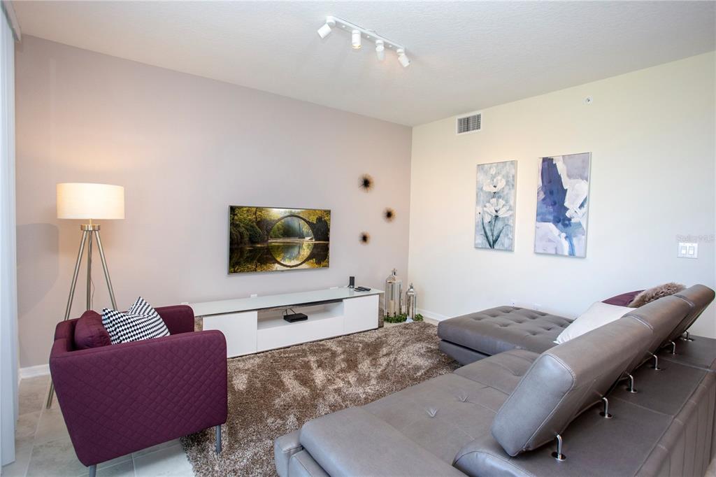 A living room features a grey sectional sofa, a purple armchair, and a wall-mounted television — 4721 CLOCK TOWER DRIVE UNIT 306, KISSIMMEE, FL