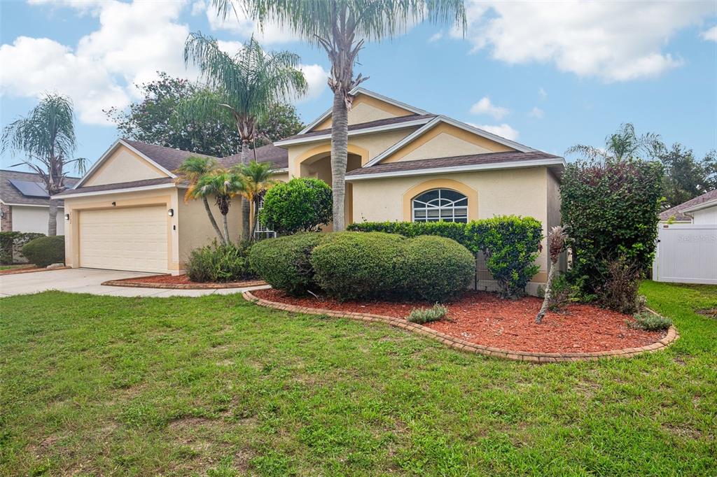 A single-story house with a beige stucco exterior, a two-car garage, and landscaped front yard — 2302 TOWERING OAKS CIRCLE, SEFFNER, FL