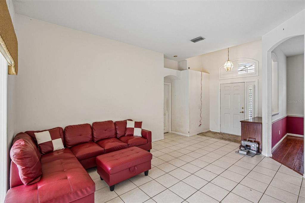 A living room features white tile flooring, a red sectional sofa, and an entryway door — 2302 TOWERING OAKS CIRCLE, SEFFNER, FL
