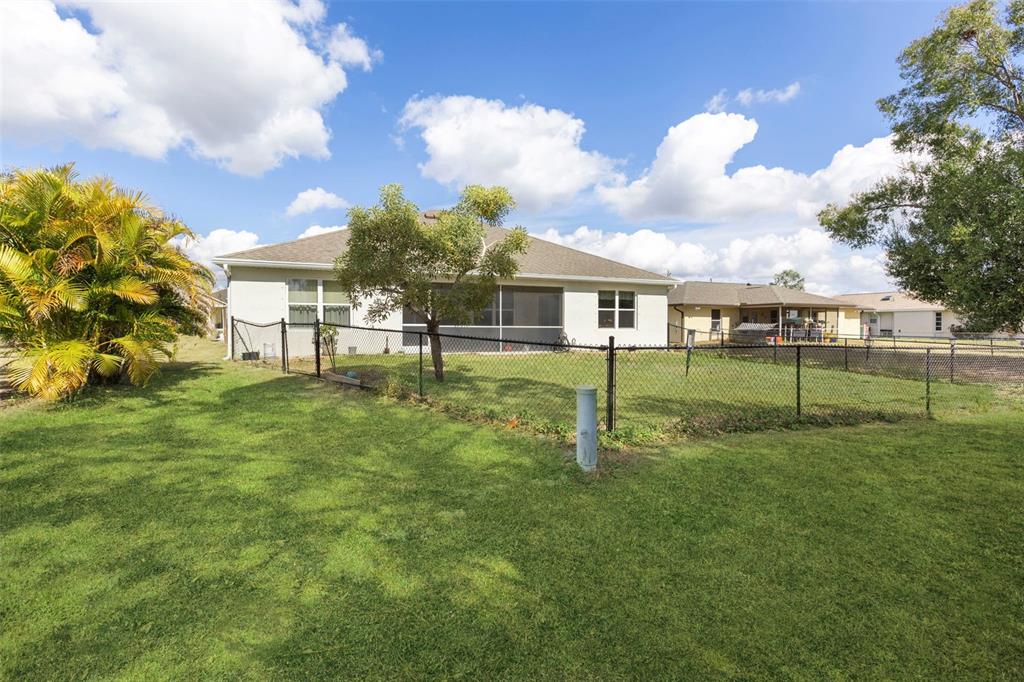 A fenced backyard features a grassy lawn, a small tree, and a house with a lanai — 25099 BOLIVAR DRIVE, PUNTA GORDA, FL