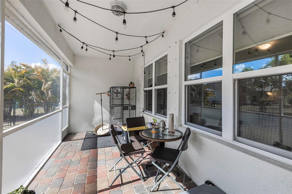 A screened-in patio features a brick floor, string lights, and a small bistro table set — 25099 BOLIVAR DRIVE, PUNTA GORDA, FL