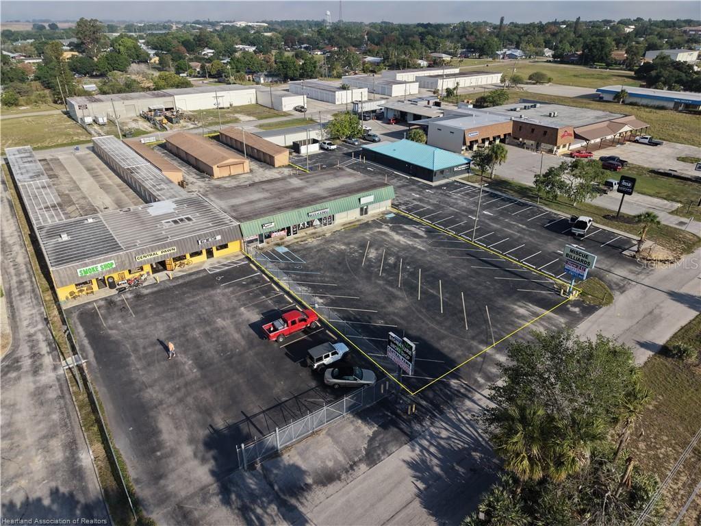 An aerial view shows a commercial strip mall with a parking lot and storage units — 708 US 27 S, LAKE PLACID, FL