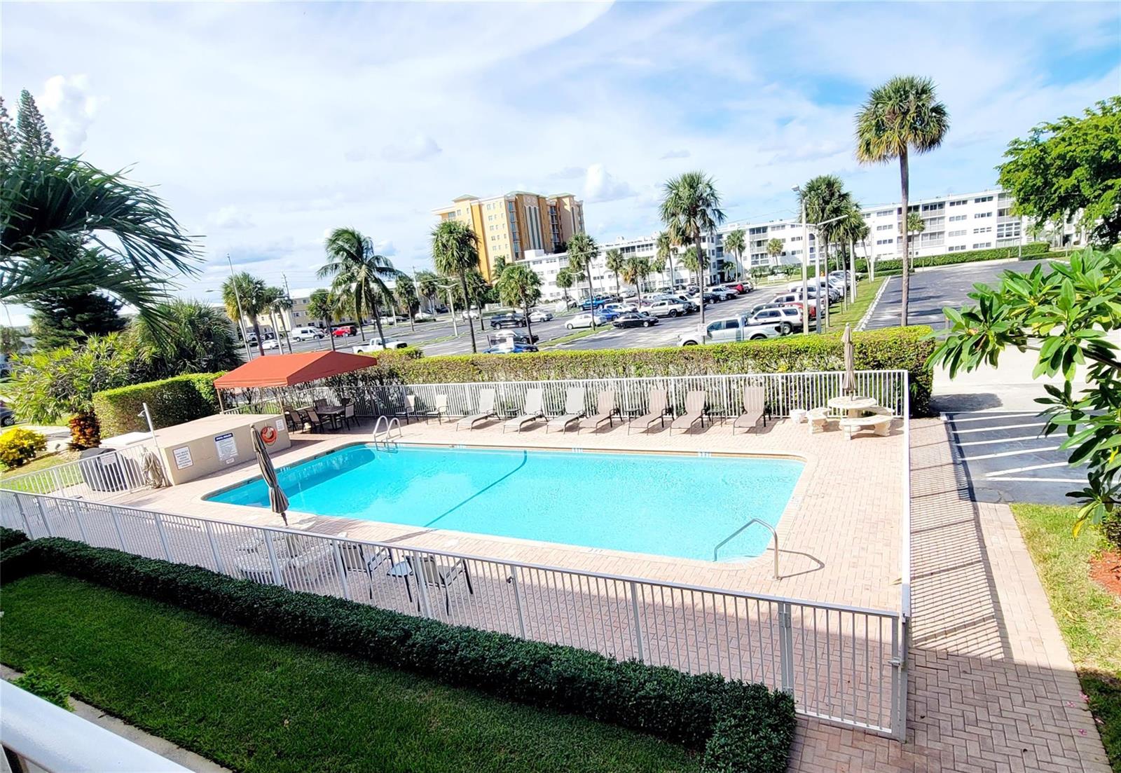 An outdoor swimming pool with lounge chairs is enclosed by a white fence — 3200 NE 7th Court # 208a, Pompano Beach FL 33062, POMPANO BEACH, FL