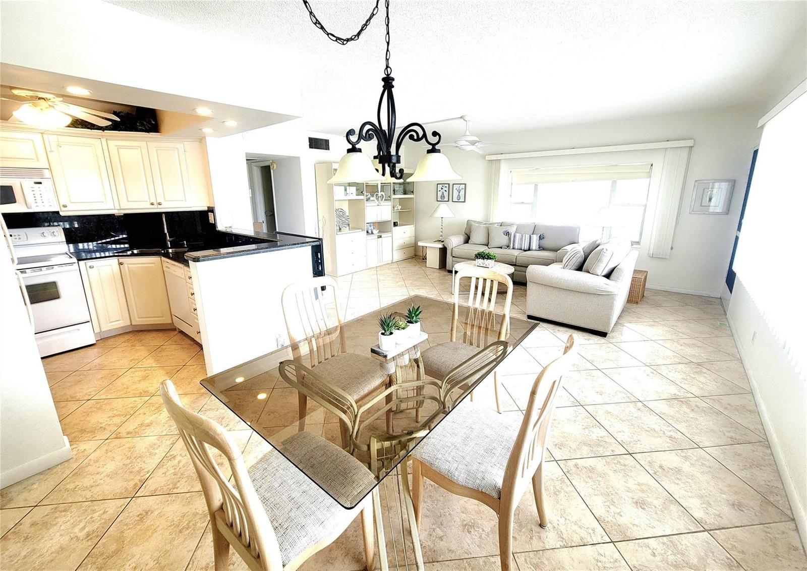 An open-concept living and dining area features tile floors, a glass-top table, and white cabinetry — 3200 NE 7th Court # 208a, Pompano Beach FL 33062, POMPANO BEACH, FL