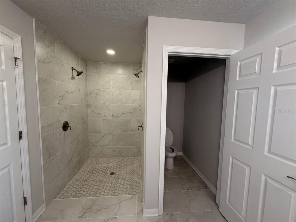 A bathroom features a tiled walk-in shower with dual showerheads and an adjacent enclosed toilet area — 110 N DUPONT TERRACE, INVERNESS, FL