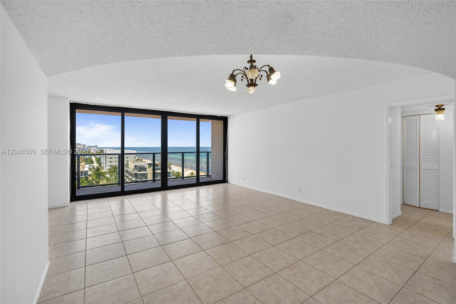 An empty living room features beige tile flooring, a vaulted ceiling, and a balcony view — 2301 S Ocean Dr # 1004, Hollywood FL 33019, HOLLYWOOD, FL