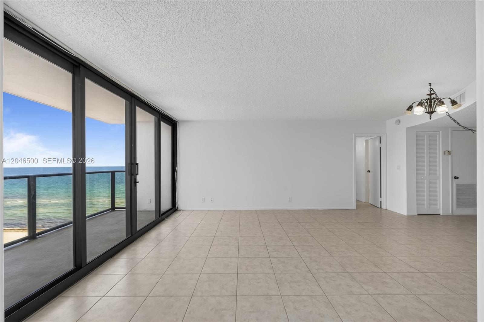 An empty room with beige tile floors, white walls, a chandelier, and sliding glass balcony doors — 2301 S Ocean Dr # 1004, Hollywood FL 33019, HOLLYWOOD, FL
