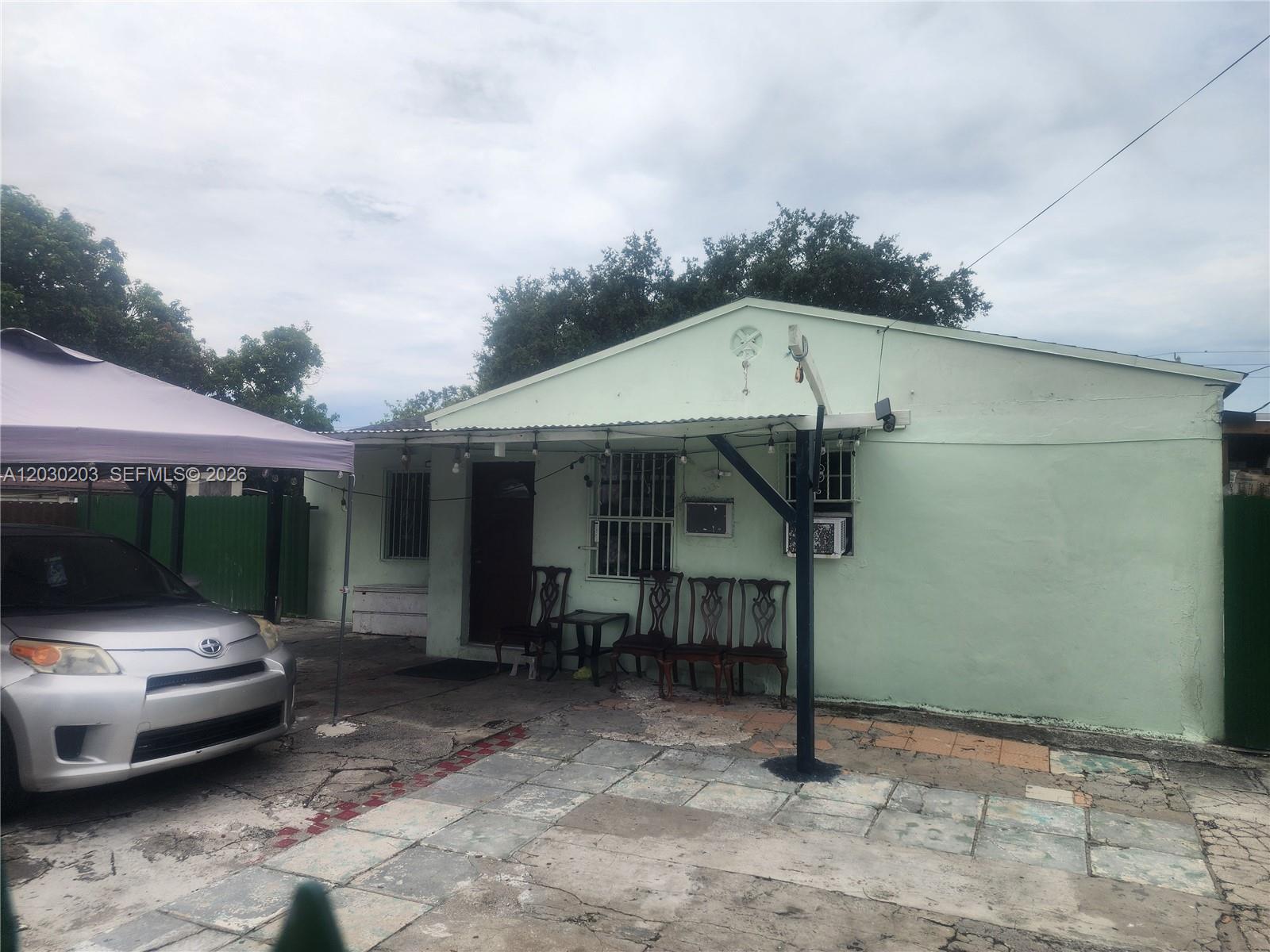 A light green house exterior features a covered patio area with chairs and a car — 2130 NW 92nd St, Miami FL 33147, MIAMI, FL
