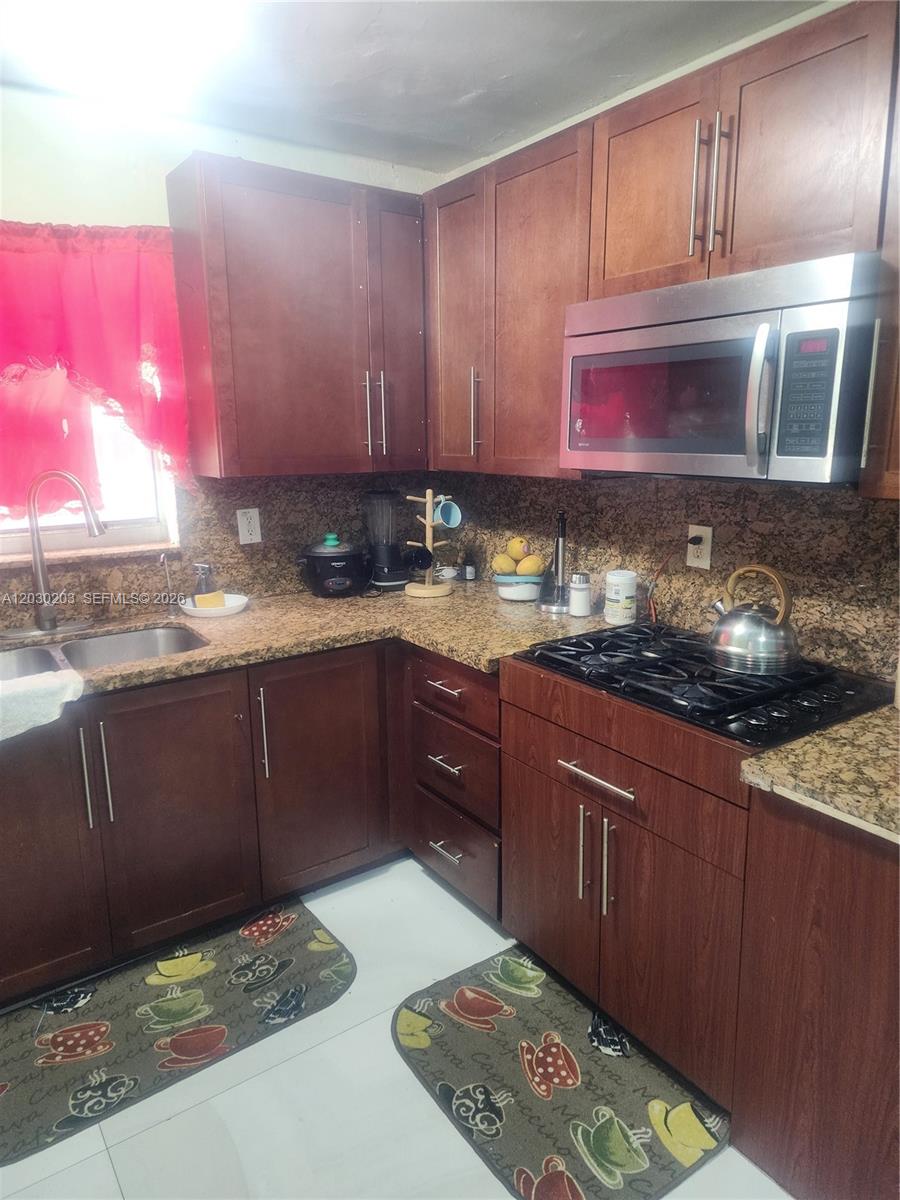 A kitchen features dark wood cabinets, granite countertops, a gas stove, and a microwave — 2130 NW 92nd St, Miami FL 33147, MIAMI, FL