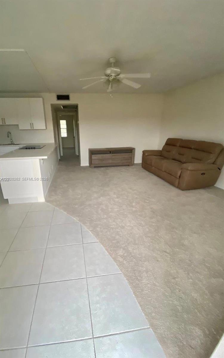 An open-concept living area features a kitchen with white cabinets, carpeted flooring, and a sofa — 335 Brighton H # 335, Boca Raton FL 33434, BOCA RATON, FL