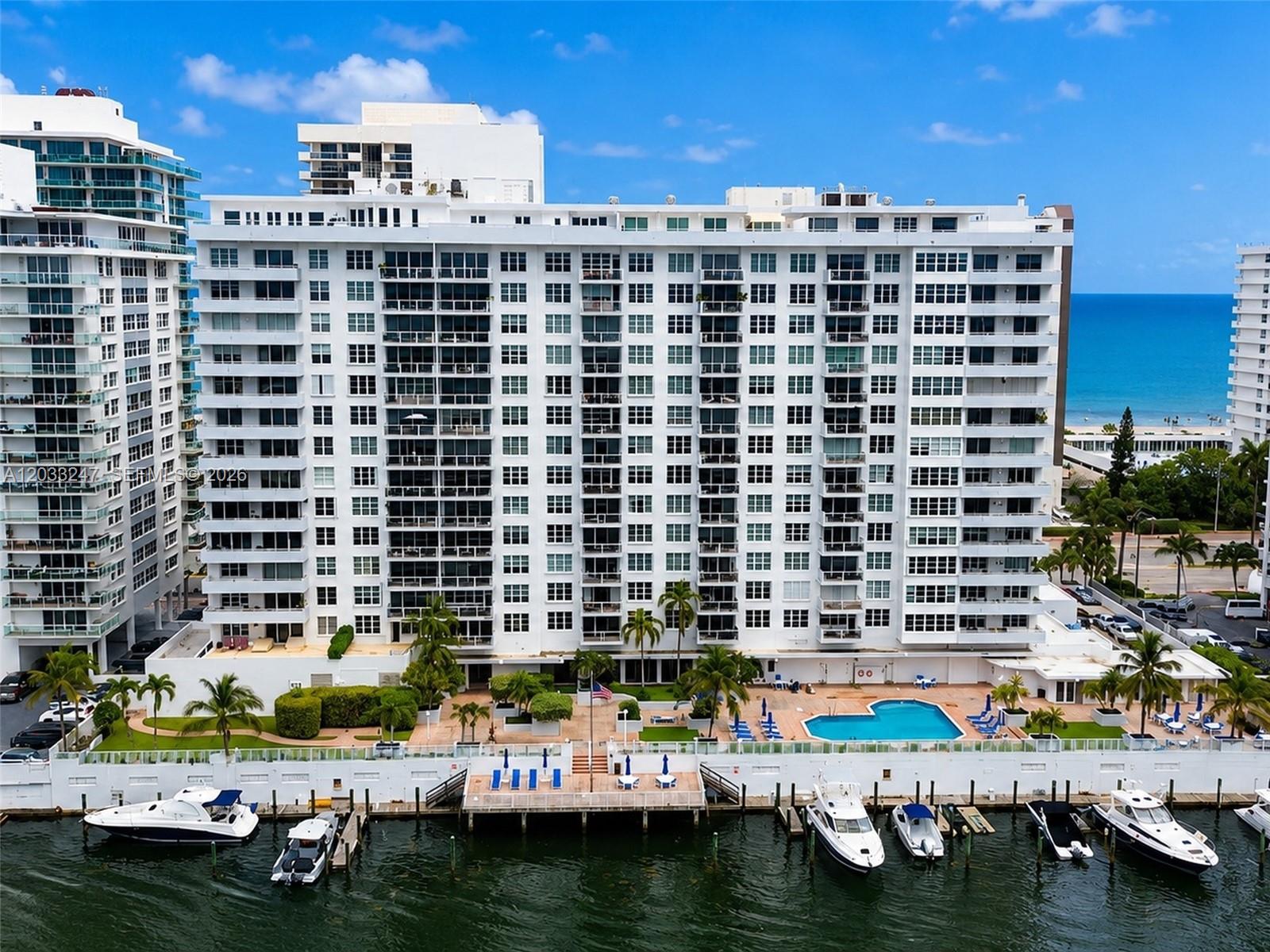 An aerial view of a white waterfront apartment building with a pool and boat docks — 5700 Collins Ave # 3A, Miami Beach FL 33140, MIAMI BEACH, FL