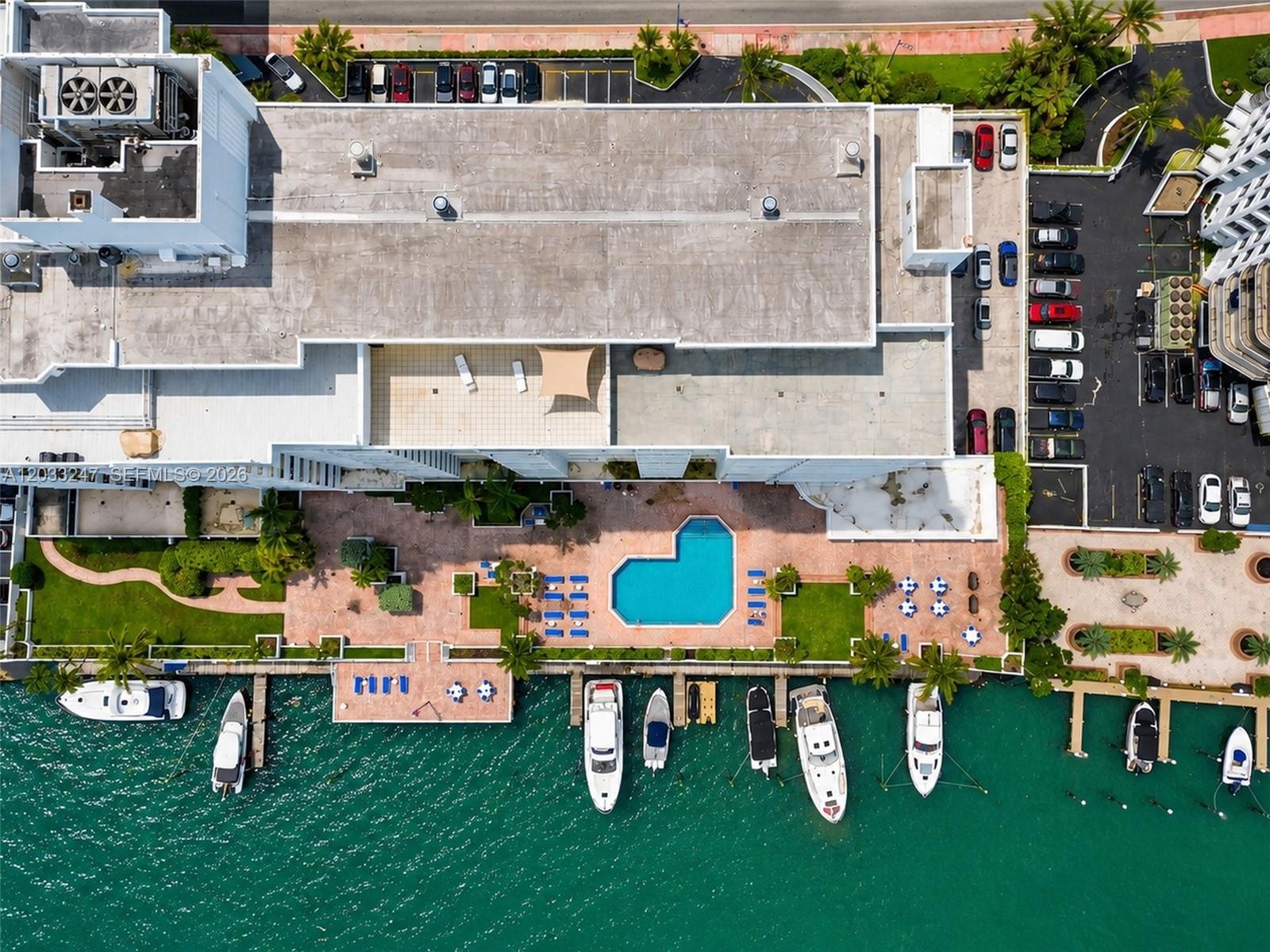 An aerial view shows a building with a pool, patio, and boat slips on water — 5700 Collins Ave # 3A, Miami Beach FL 33140, MIAMI BEACH, FL