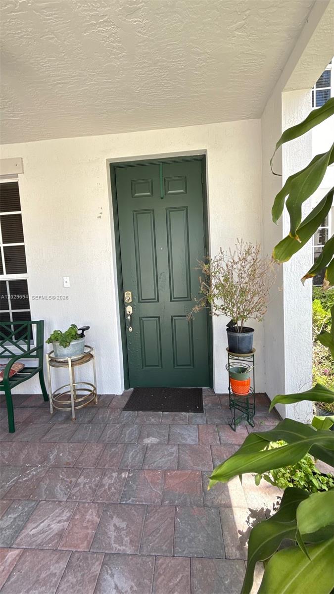 A green front door is centered on a covered patio with tiled flooring and plants — 9213 SW 170th Ave, Miami FL 33196, MIAMI, FL