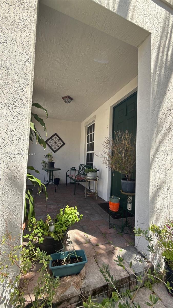 A covered entryway features a dark green door, tiled flooring, and several potted plants — 9213 SW 170th Ave, Miami FL 33196, MIAMI, FL