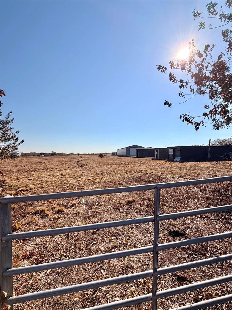 A metal gate in the foreground overlooks a dry, grassy field with several outbuildings — 3970 NE 80th Avenue, Okeechobee FL 34972, OKEECHOBEE, FL