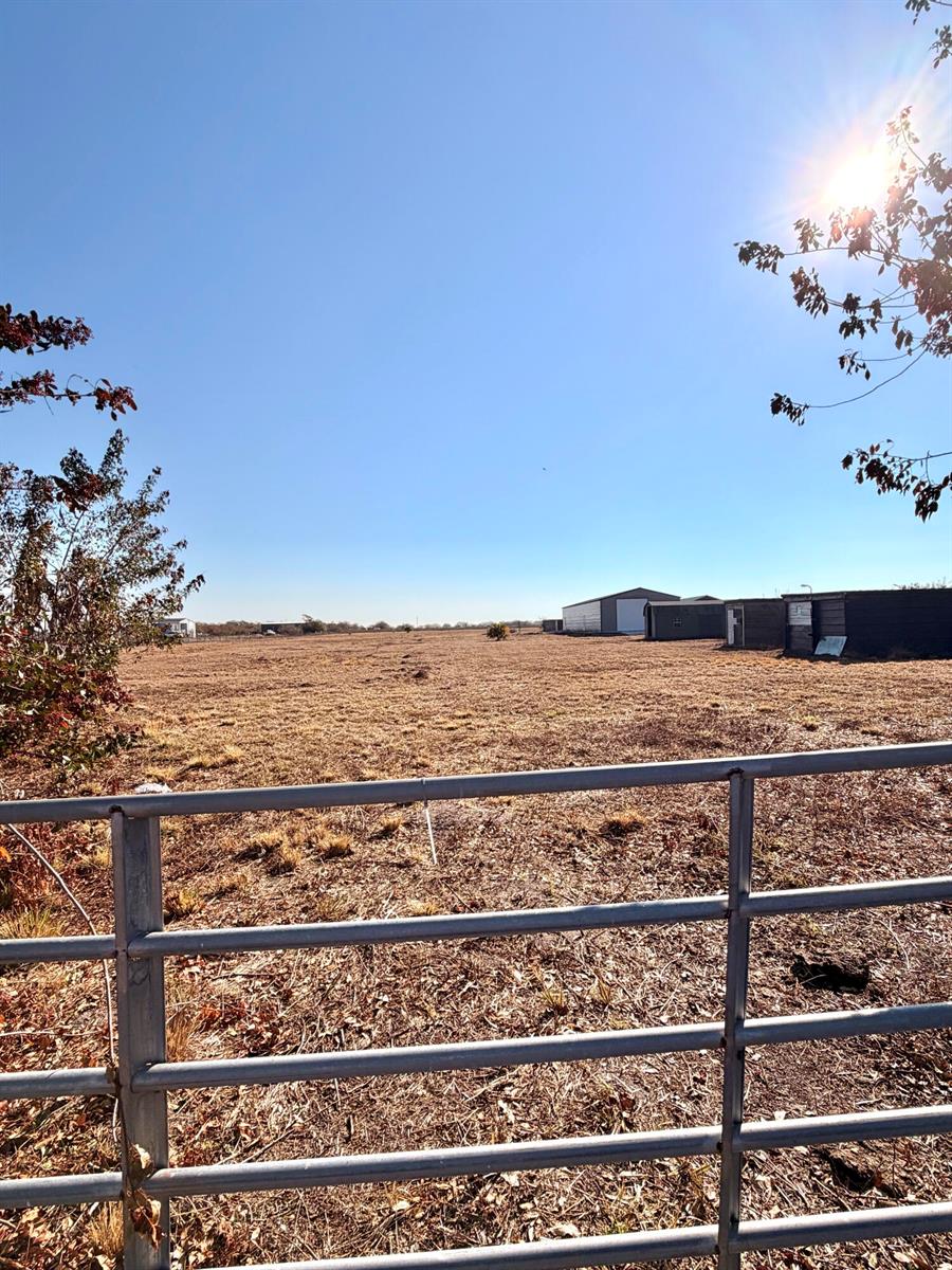 A metal gate overlooks a large, dry, open field with several storage buildings in the distance — 3970 NE 80th Avenue, Okeechobee FL 34972, OKEECHOBEE, FL