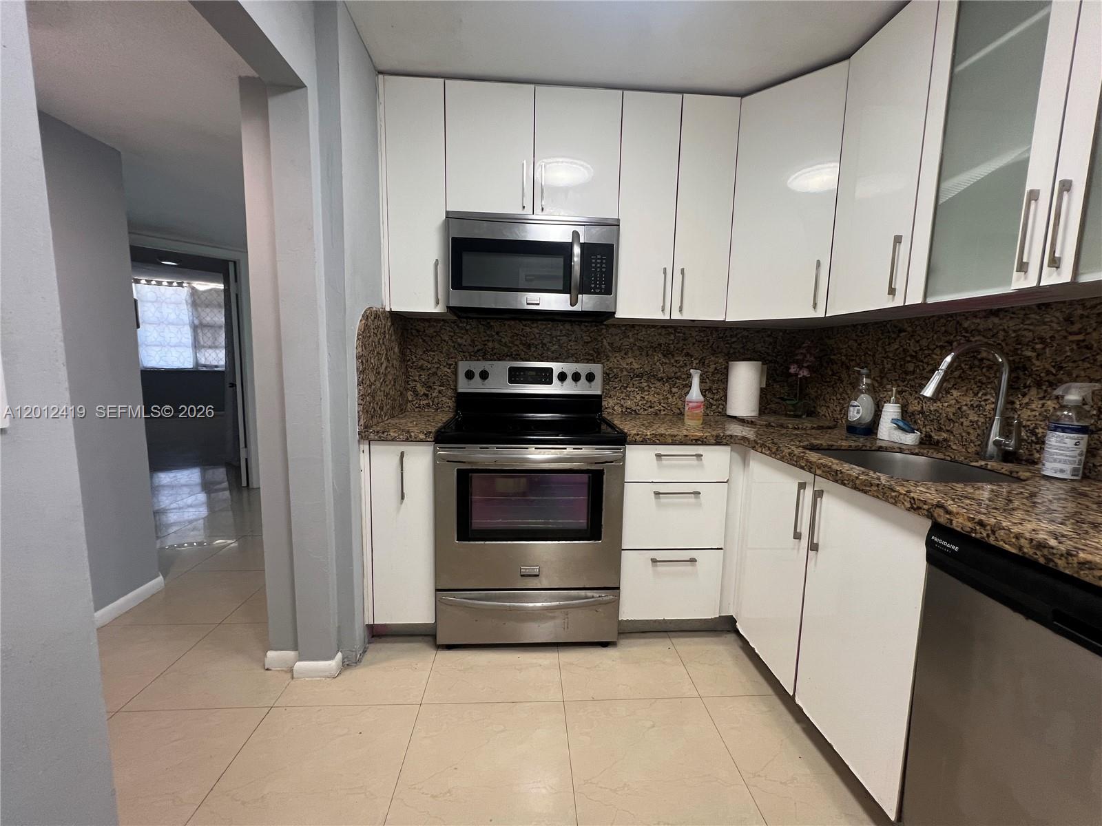 A kitchen features white cabinets, stainless steel appliances, and granite countertops with tile flooring — 1801 S Ocean Dr # 535, Hallandale Beach FL 33009, HALLANDALE BEACH, FL