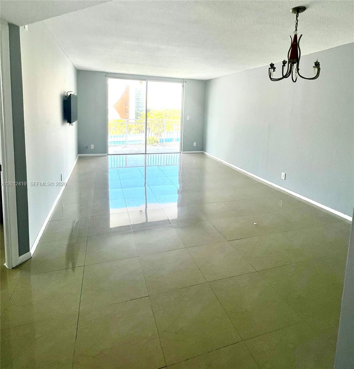 An empty living room features light-colored tile flooring, pale blue walls, and a sliding glass door — 1801 S Ocean Dr # 535, Hallandale Beach FL 33009, HALLANDALE BEACH, FL