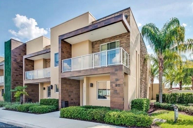 A modern two-story townhouse exterior features tan stucco, stone accents, and glass-railed balconies — 7651 AMAZONAS STREET, KISSIMMEE, FL