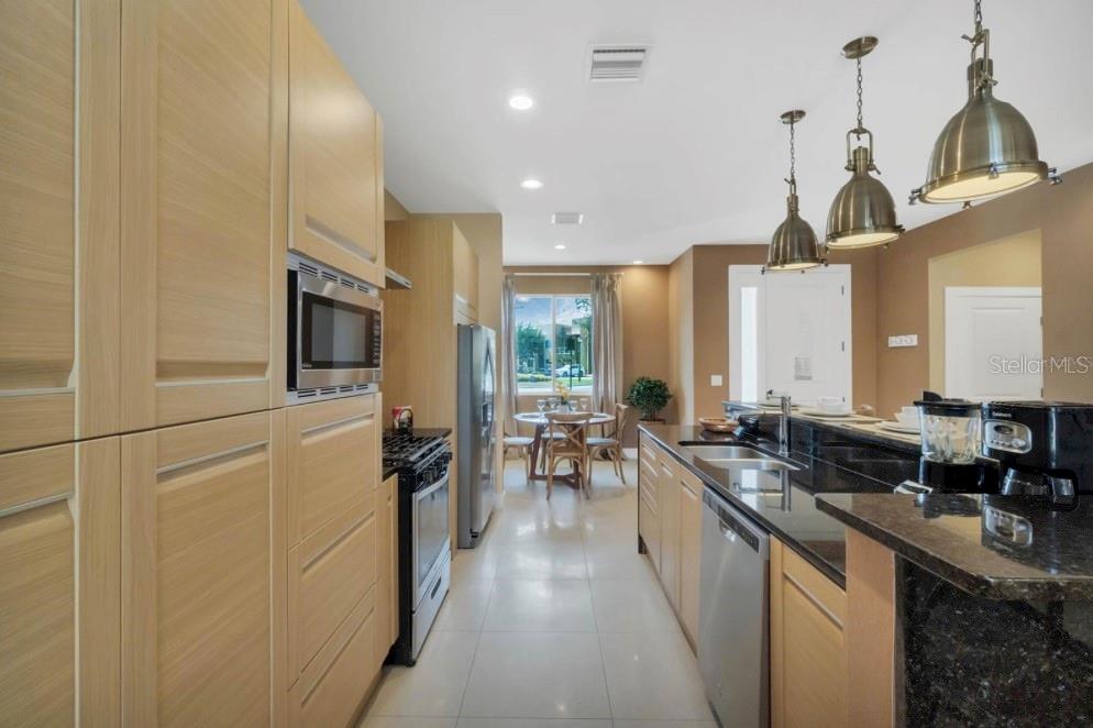 A modern kitchen features light wood cabinetry, black granite countertops, and stainless steel appliances — 7651 AMAZONAS STREET, KISSIMMEE, FL