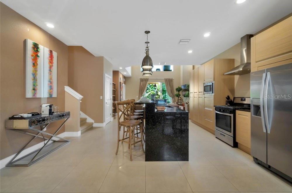 A modern kitchen features light wood cabinets, a black granite island, and stainless steel appliances — 7651 AMAZONAS STREET, KISSIMMEE, FL