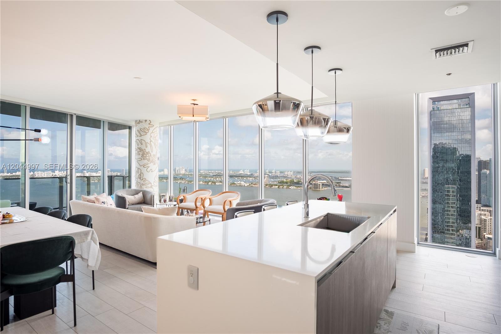 A modern kitchen island with a sink overlooks a living area with floor-to-ceiling water views — 2900 NE 7th Ave # 4307, Miami FL 33137, MIAMI, FL