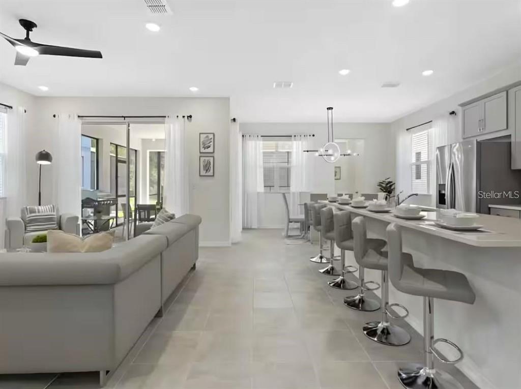 A modern open-concept living room and kitchen featuring light tile floors and bar seating — 1929 TROPICAL PALMS CIRCLE, KISSIMMEE, FL