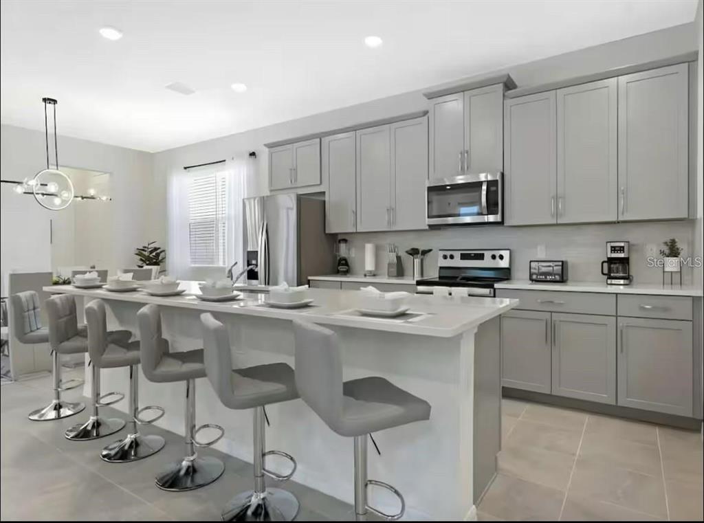 A modern kitchen features gray cabinetry, a large island with bar seating, and stainless appliances — 1929 TROPICAL PALMS CIRCLE, KISSIMMEE, FL