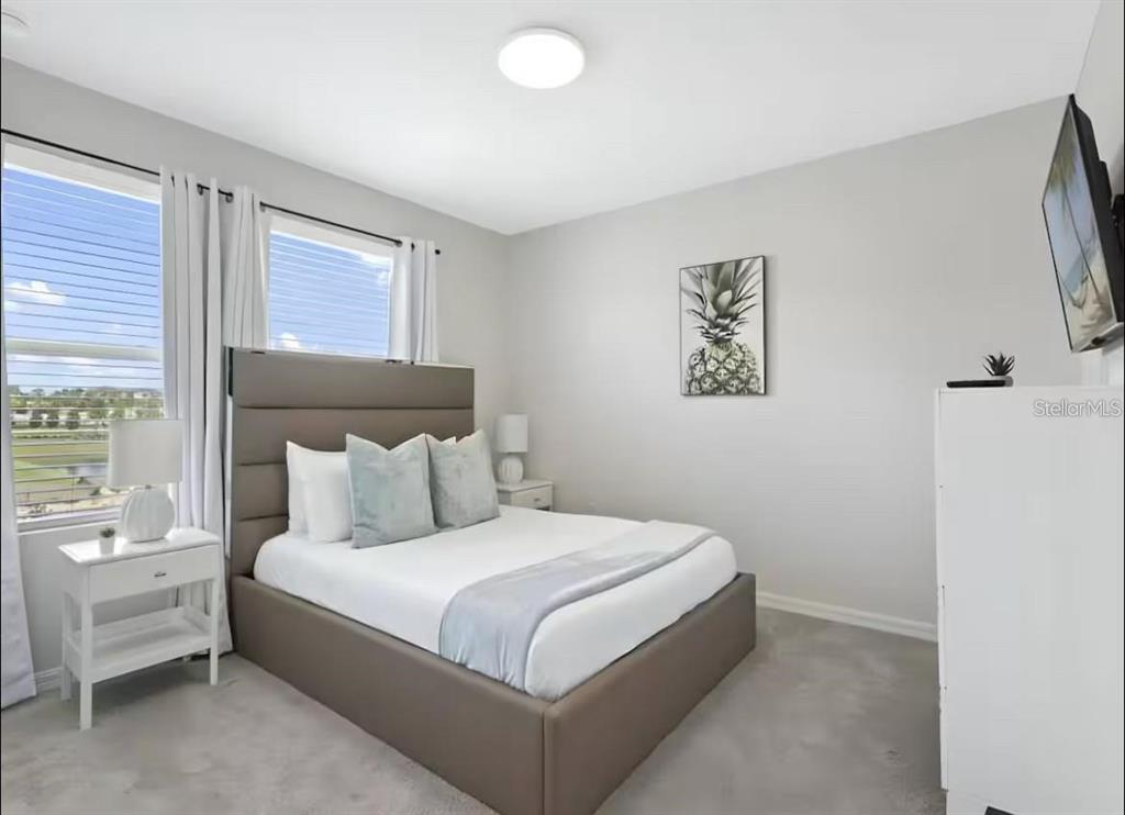 A bedroom with a gray upholstered bed, white nightstands, and a pineapple wall art piece — 1929 TROPICAL PALMS CIRCLE, KISSIMMEE, FL