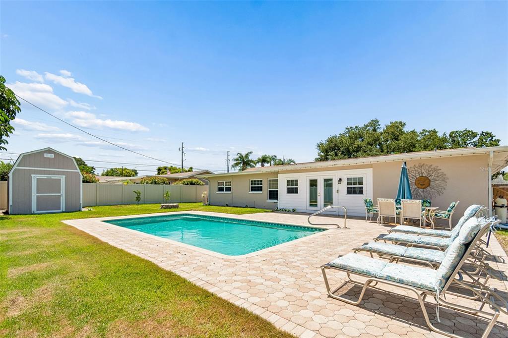 A backyard features a rectangular swimming pool, a paved patio, lounge chairs, and a storage shed — 14006 STARBOARD DRIVE, SEMINOLE, FL