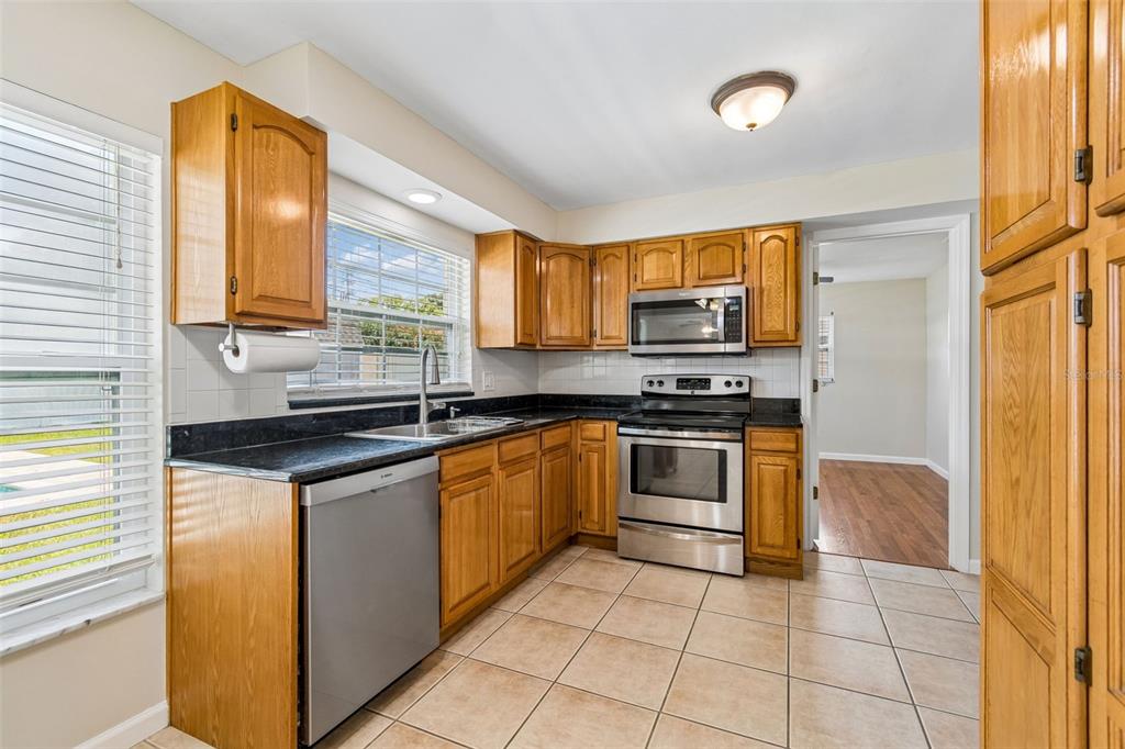 A kitchen features oak cabinets, stainless steel appliances, black countertops, and light-colored floor tiles — 14006 STARBOARD DRIVE, SEMINOLE, FL
