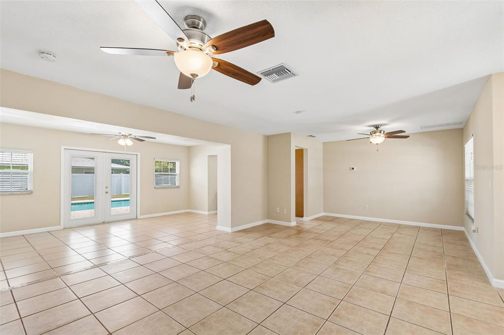 An open-concept living area features beige tile flooring, two ceiling fans, and glass patio doors — 14006 STARBOARD DRIVE, SEMINOLE, FL