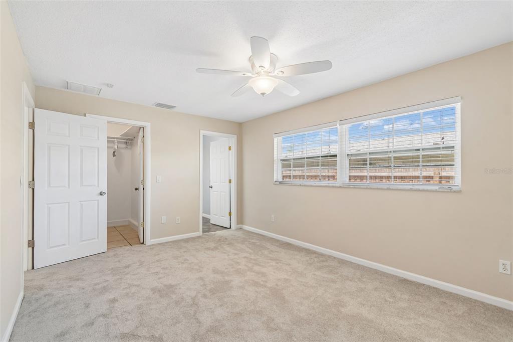 A bedroom with beige walls, gray carpet, a ceiling fan, and two open doorways — 14006 STARBOARD DRIVE, SEMINOLE, FL