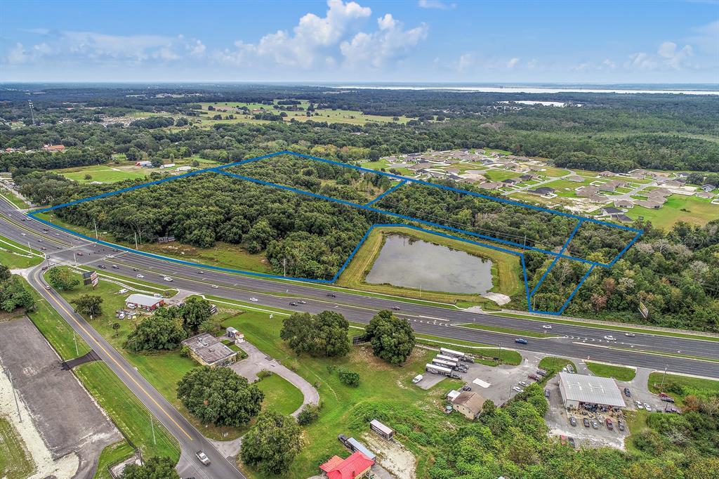 An aerial view shows a wooded plot of land outlined in blue next to a pond — 2631 US-441, FRUITLAND PARK, FL