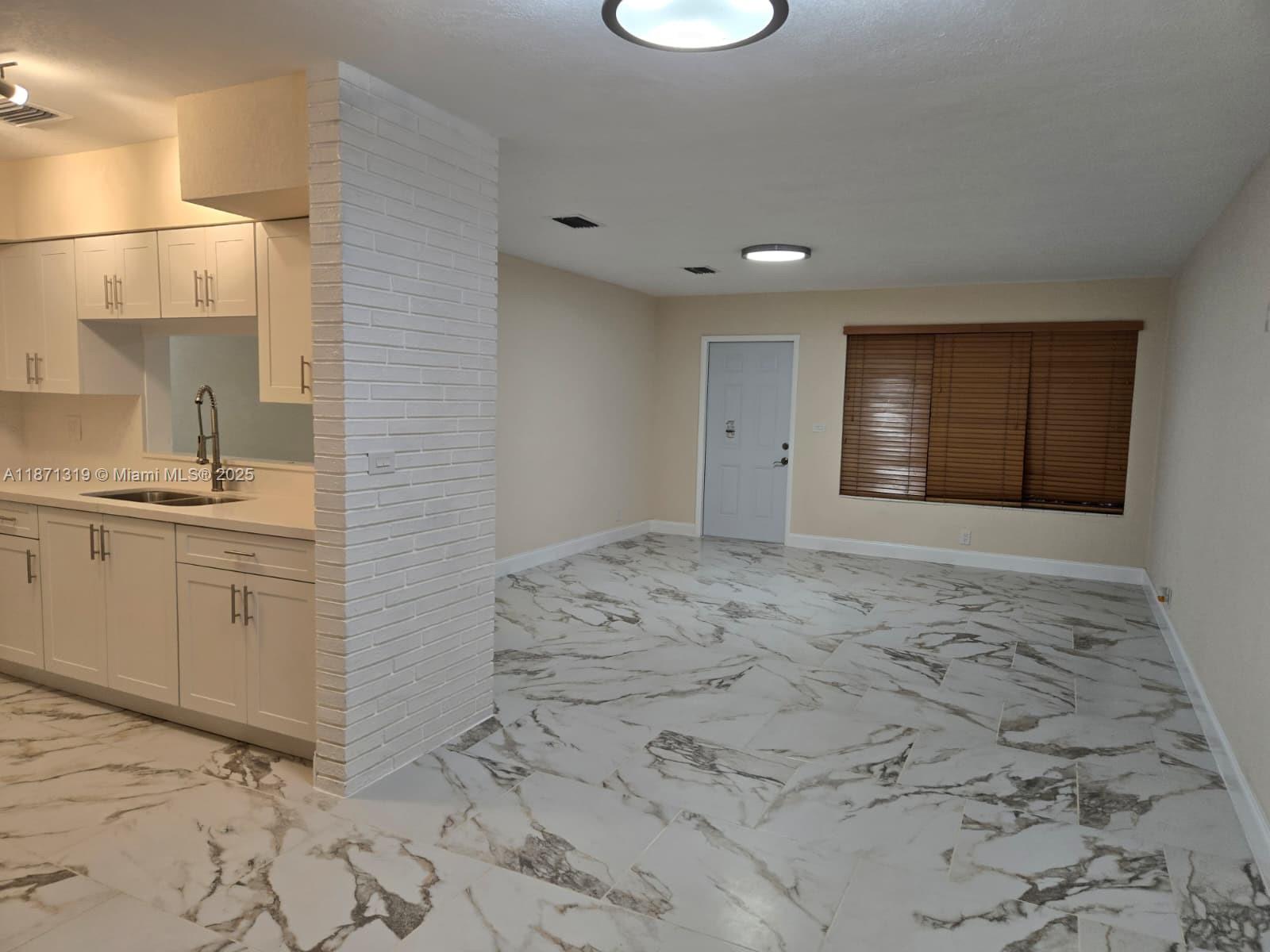An open-concept kitchen and living area features white cabinets, a brick pillar, and marble-patterned flooring — 6751 Meade St, Hollywood FL 33024, HOLLYWOOD, FL
