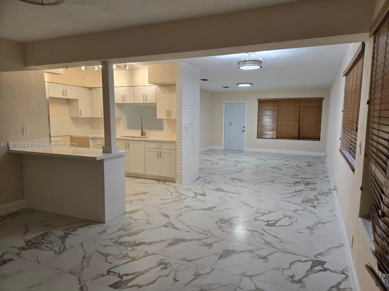 An open-concept kitchen and living area features white cabinetry and marble-patterned tile flooring — 6751 Meade St, Hollywood FL 33024, HOLLYWOOD, FL