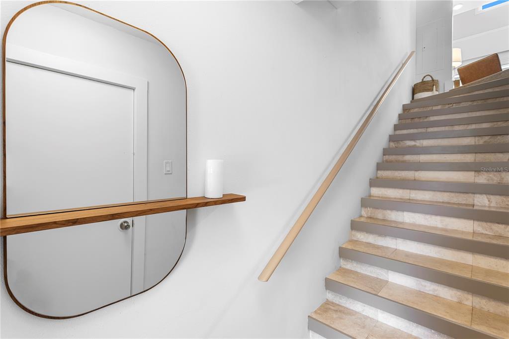 A staircase with light-colored tile steps and a wooden handrail sits beside a wall mirror — 360 PINELLAS BAYWAY S UNIT I, TIERRA VERDE, FL
