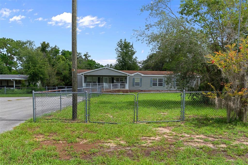 A single-story manufactured home with a front porch sits behind a chain-link fence — 7351 W HADENOTTER LANE, HOMOSASSA, FL