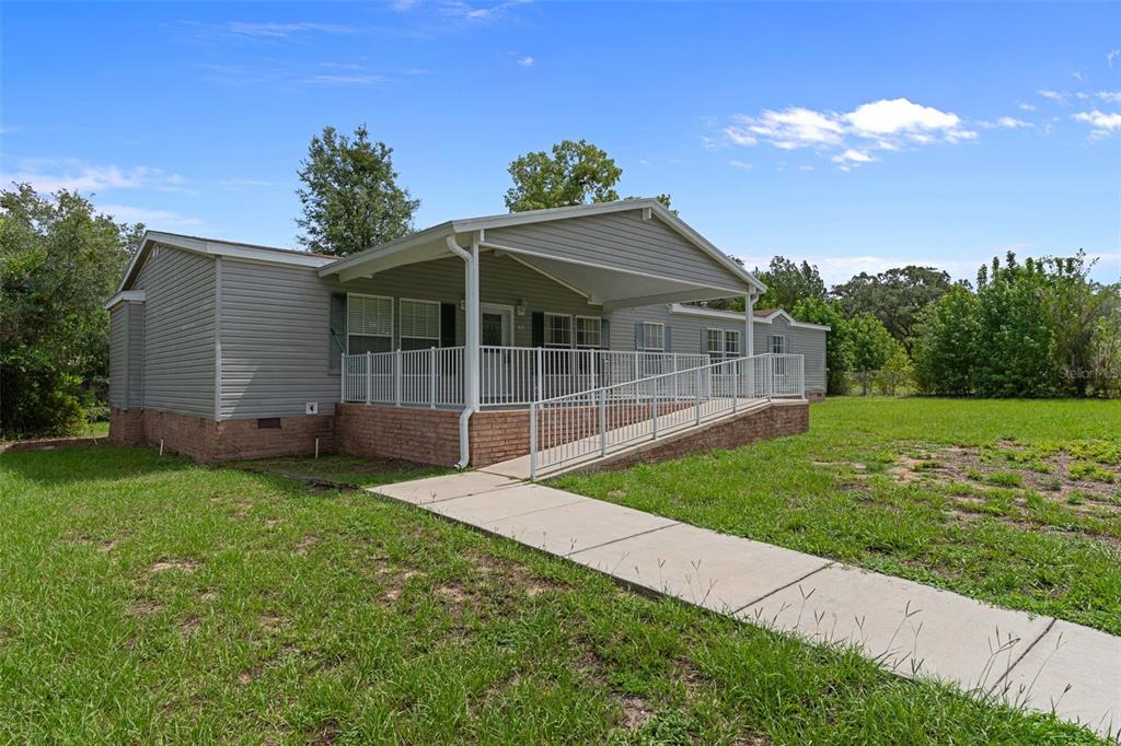 A gray manufactured home features a brick foundation, a covered porch, and a concrete ramp — 7351 W HADENOTTER LANE, HOMOSASSA, FL