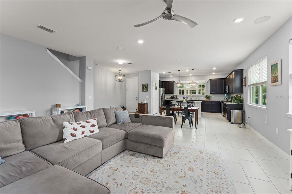 An open-concept living room with a gray sectional sofa flows into a kitchen with dark cabinetry — 13755 BRAVANTE ALLEY, WINDERMERE, FL