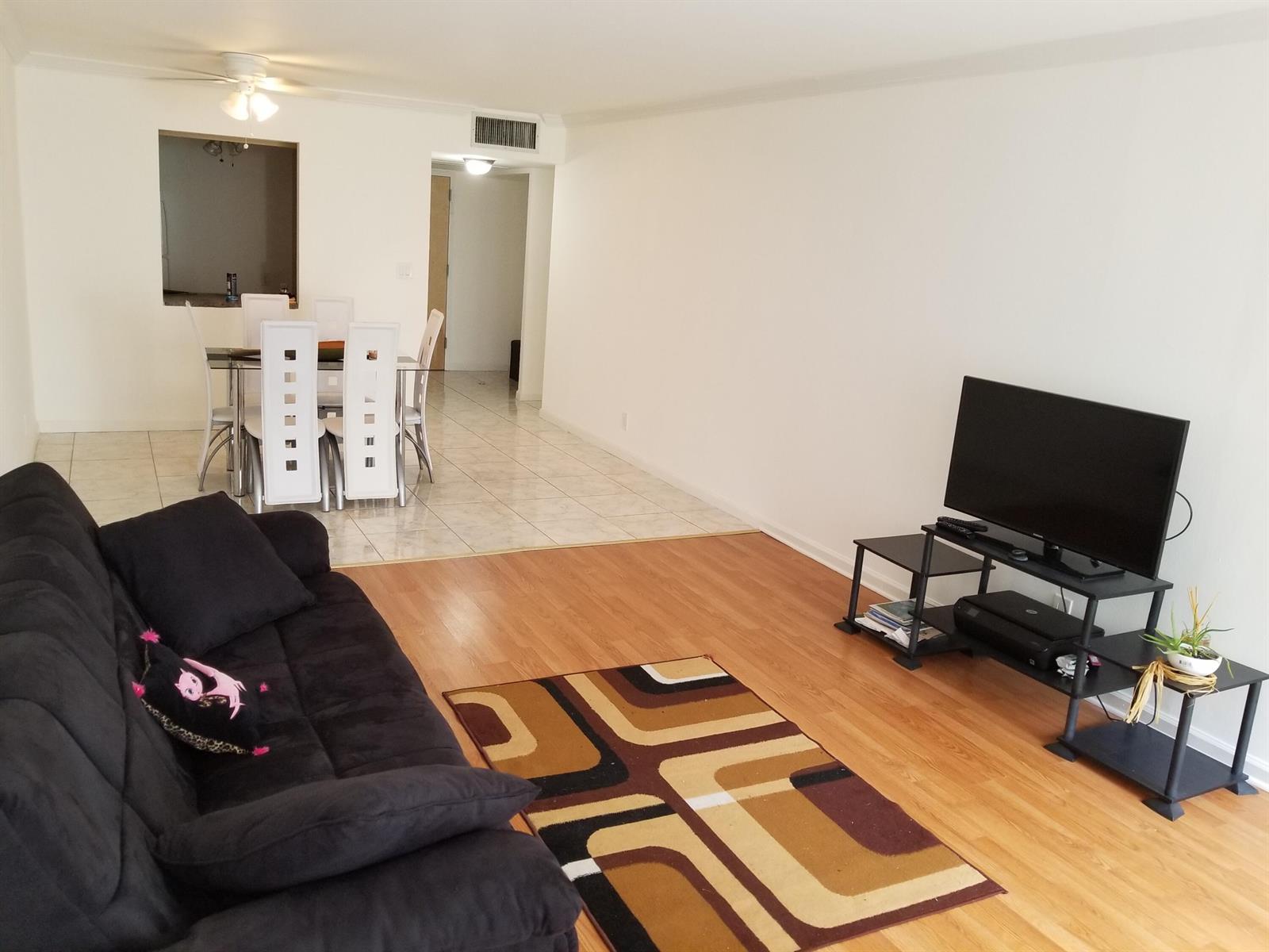 A living room with wood-look flooring, a black sofa, and an adjacent tiled dining area — 851 Three Islands Boulevard # 105, Hallandale Beach FL 33009, HALLANDALE BEACH, FL