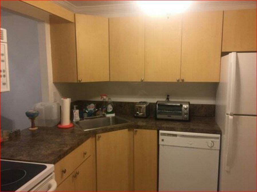 A kitchen features light wood cabinets, dark laminate countertops, and white appliances — 851 Three Islands Boulevard # 105, Hallandale Beach FL 33009, HALLANDALE BEACH, FL