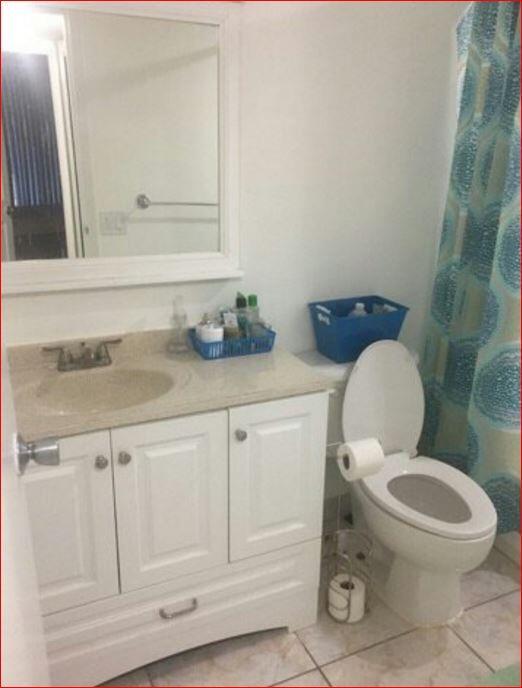 A bathroom features a white vanity with a beige countertop, a mirror, and a toilet — 851 Three Islands Boulevard # 105, Hallandale Beach FL 33009, HALLANDALE BEACH, FL
