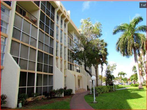 A multi-story apartment building with screened balconies sits next to a sidewalk and palm trees — 851 Three Islands Boulevard # 105, Hallandale Beach FL 33009, HALLANDALE BEACH, FL