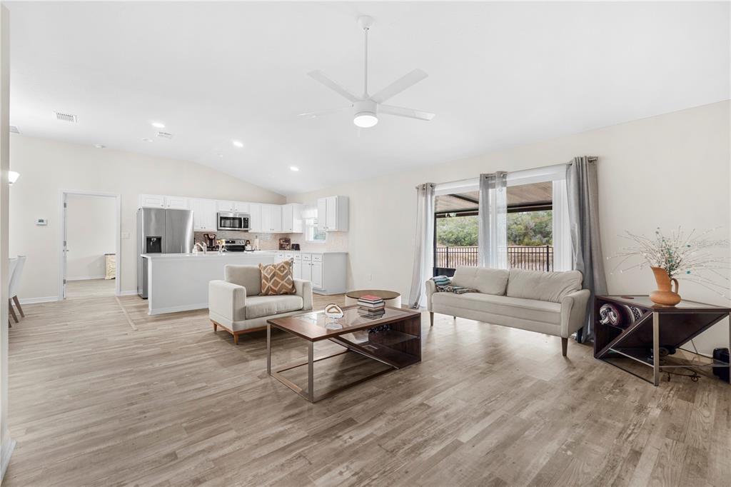 An open-concept living room features light wood-look flooring, a white kitchen, and a ceiling fan — 3321 SW 153RD PLACE ROAD, OCALA, FL