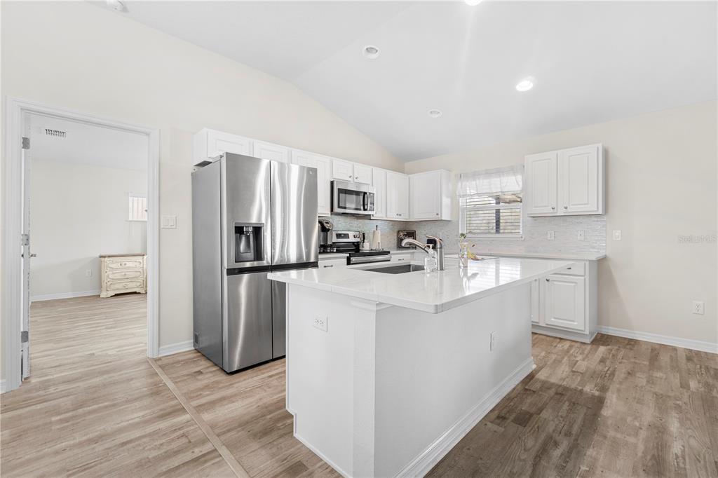 A white kitchen features a stainless steel refrigerator, a center island, and light wood flooring — 3321 SW 153RD PLACE ROAD, OCALA, FL