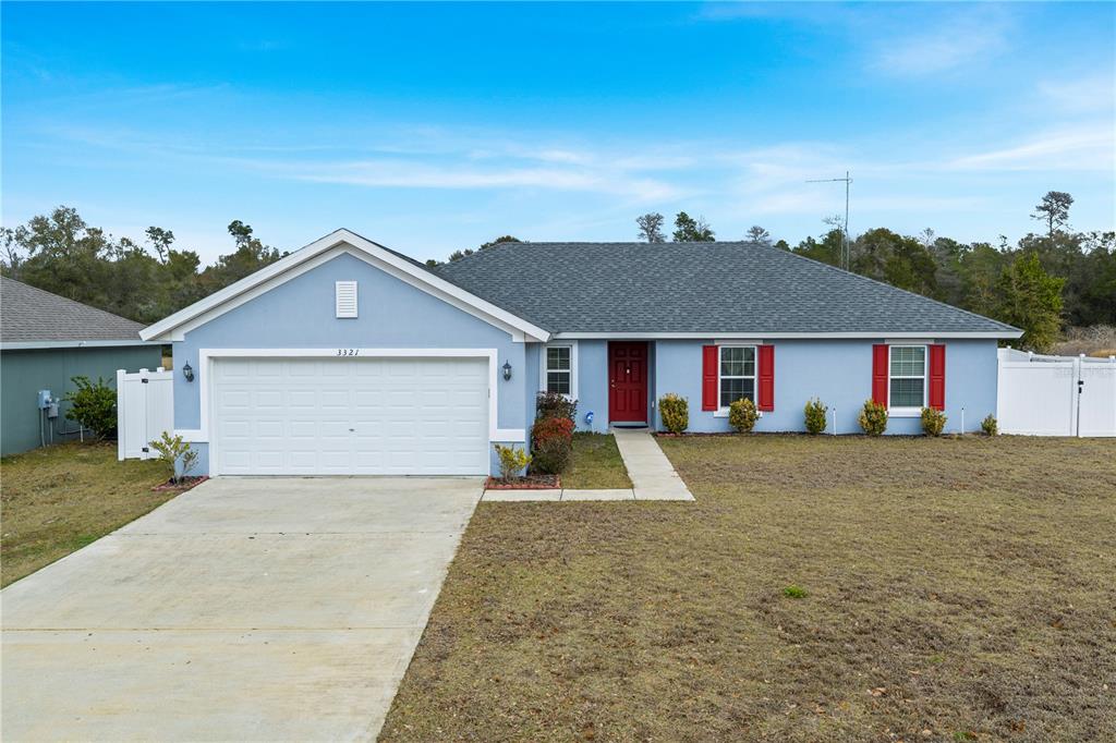 A single-story light blue house with a two-car garage, red front door, and red shutters — 3321 SW 153RD PLACE ROAD, OCALA, FL