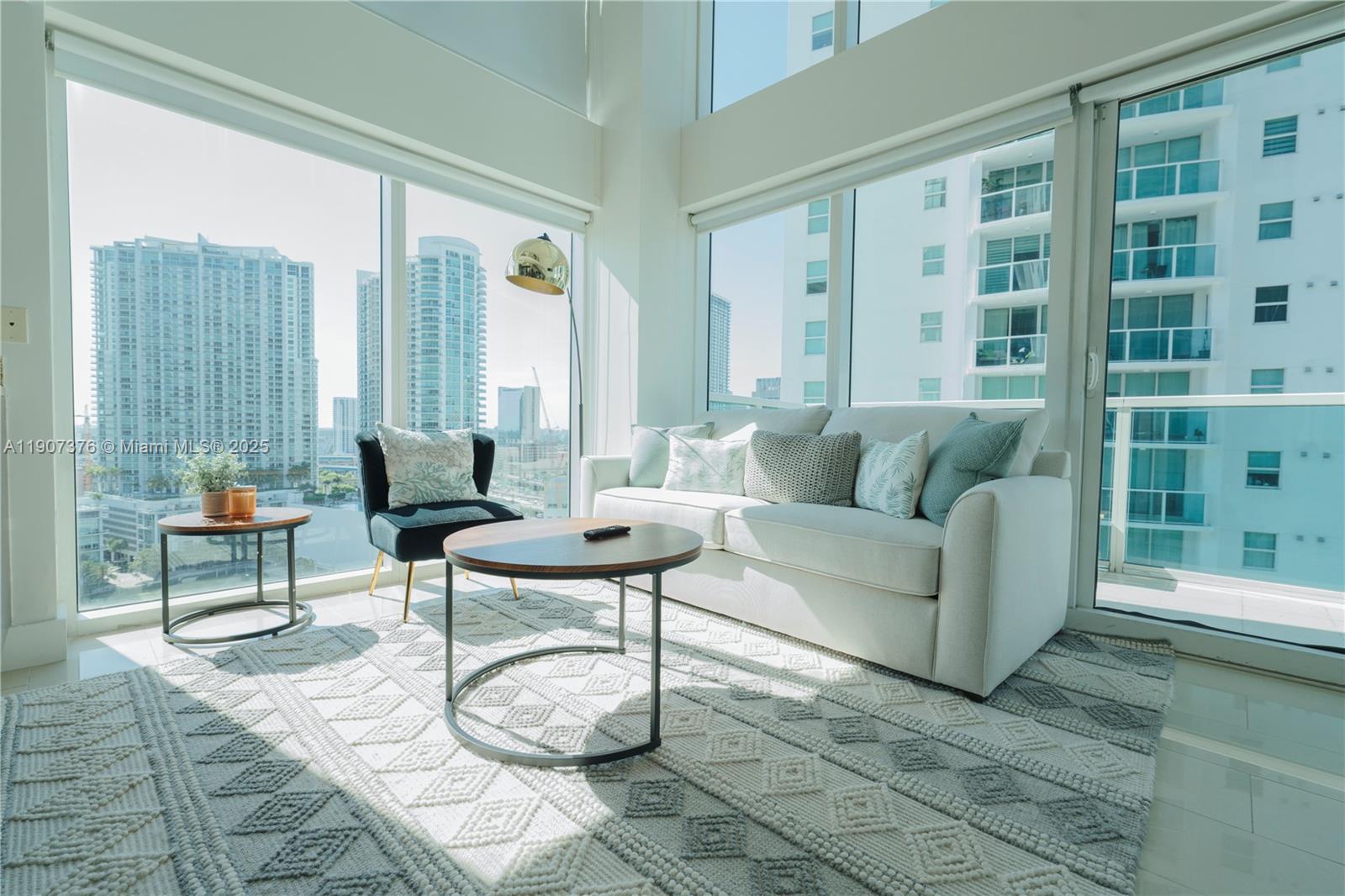 A bright living room features floor-to-ceiling windows, a white sofa, and city views — 41 SE 5th St # 1217, Miami FL 33131, MIAMI, FL
