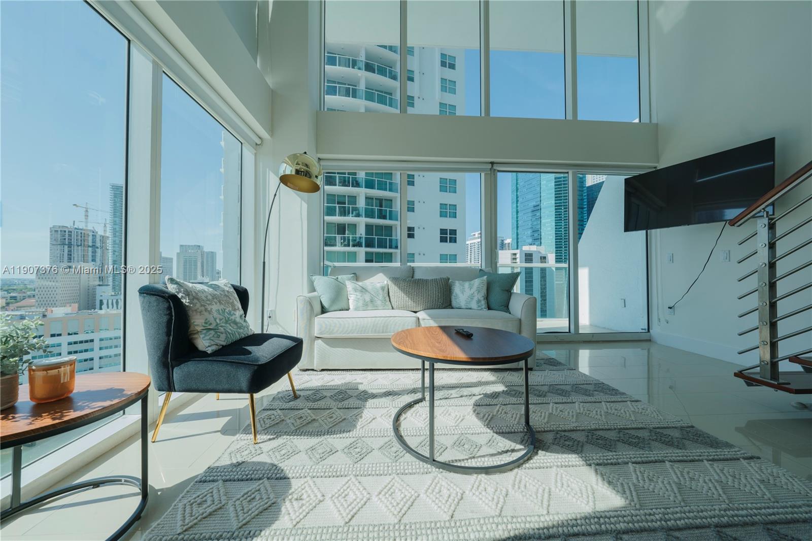 A modern living room features floor-to-ceiling windows, a white sofa, and a city view — 41 SE 5th St # 1217, Miami FL 33131, MIAMI, FL